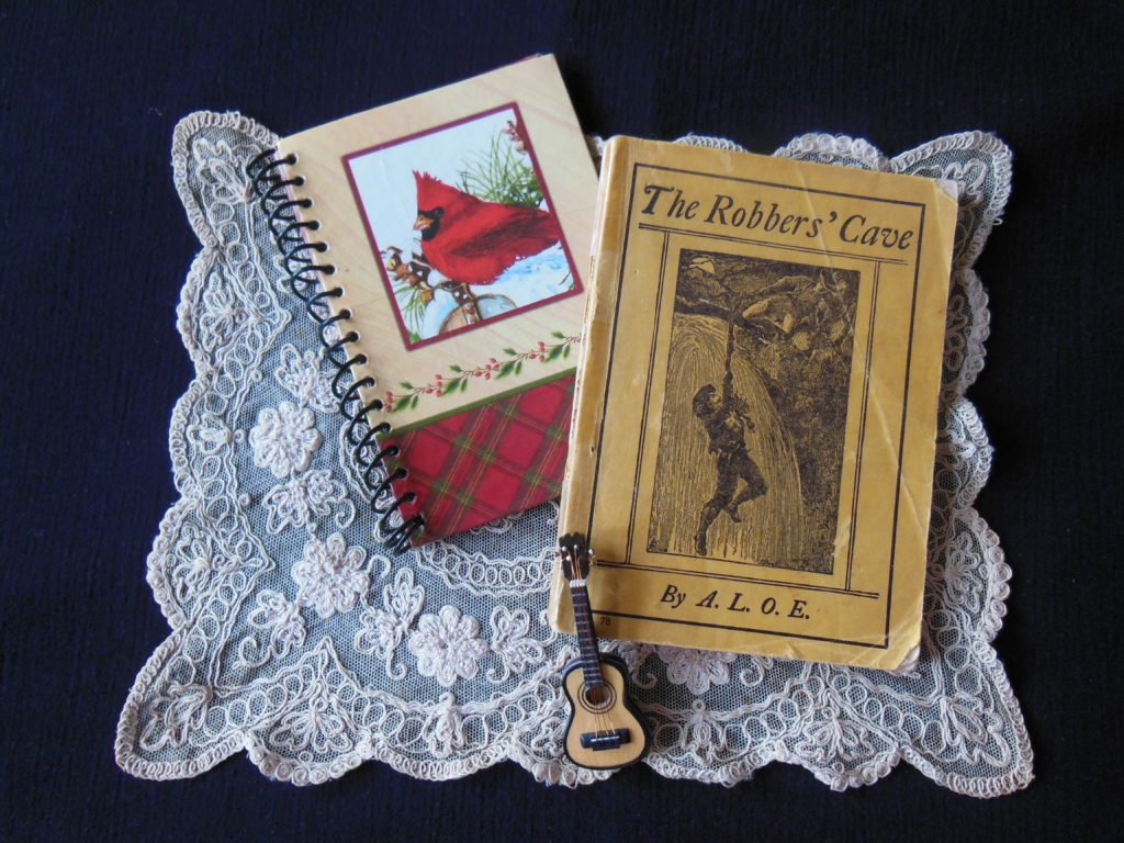 a book, a notebook, and a miniature guitar laying on a lace doily