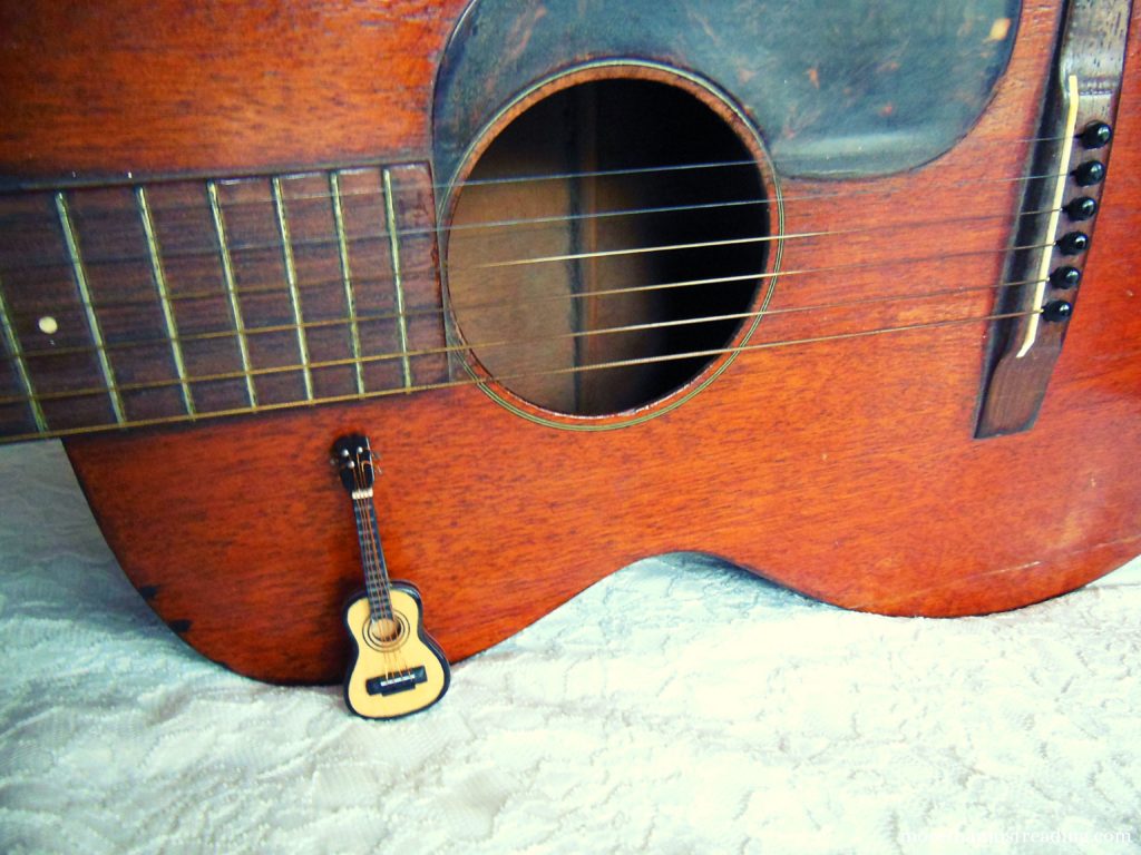 A miniature guitar leaning against the head of a full-size guitar