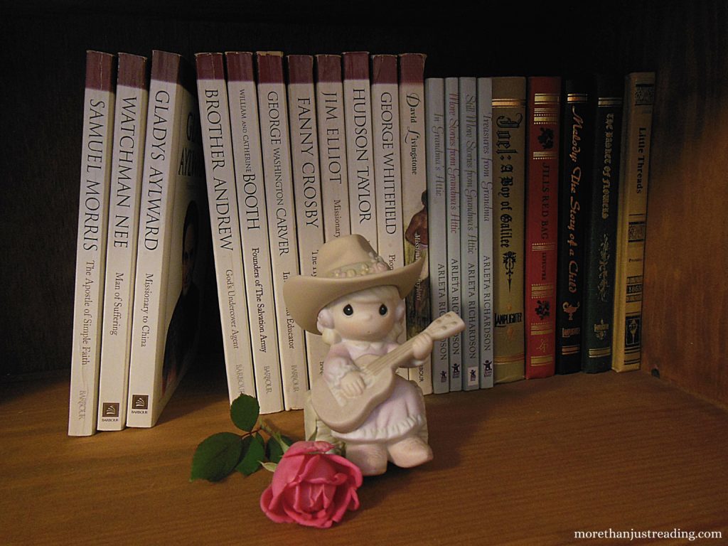 books on a shelf with a precious moments figurine and a pink rose in front of them