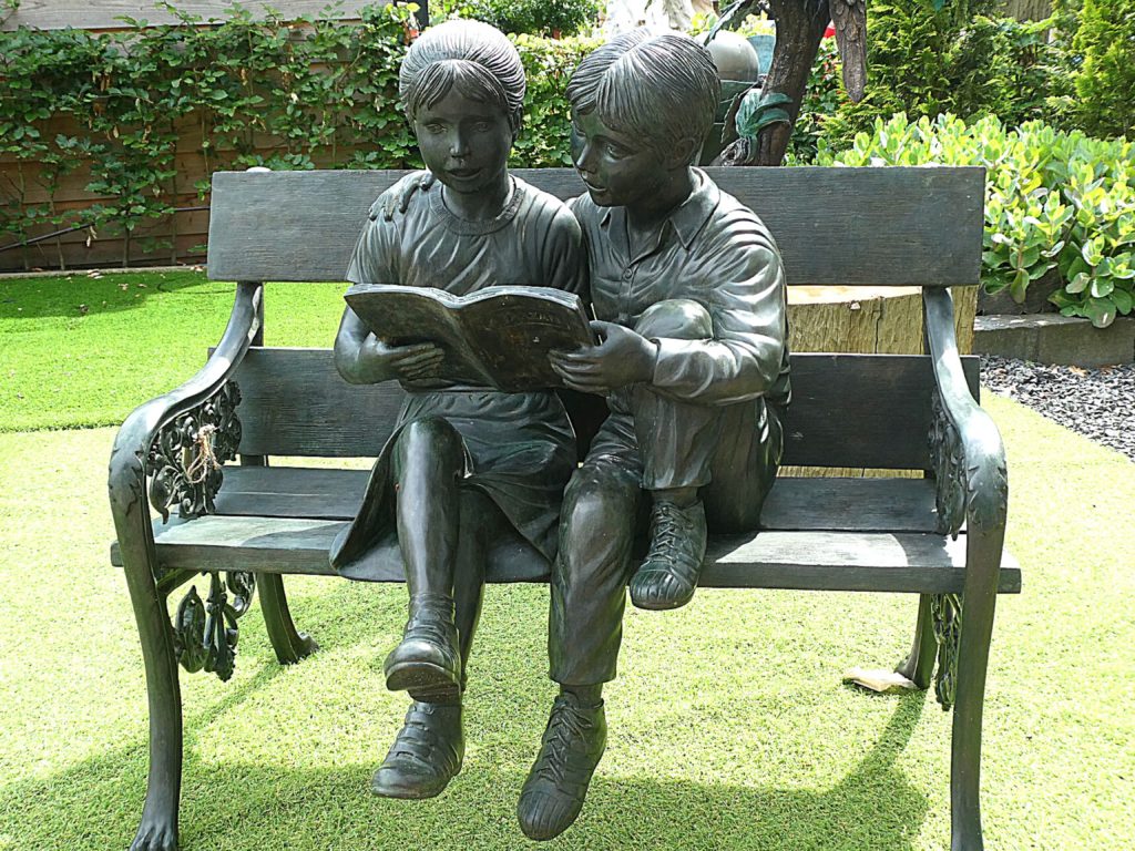 Statue of a boy and a girl sitting on a bench reading